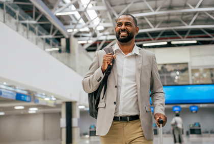 Business traveler with suit jacket over shoulder rolling luggage in spacious airport concourse