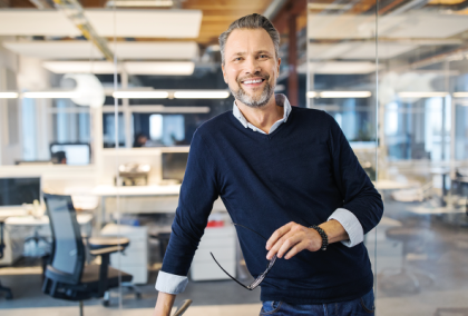 Bearded man in navy sweater leaning on desk in bright modern office, smiling