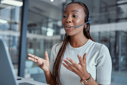 Smiling Black woman in headset gesturing during a video call in a modern office
