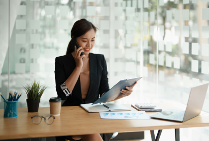 Businesswoman at desk talking on phone and reviewing documents in a bright office
