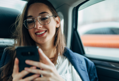 Person sitting in car backseat wearing earbuds and holding a smartphone