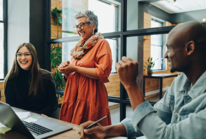 Senior woman in orange dress leading a meeting with two colleagues in a modern office
