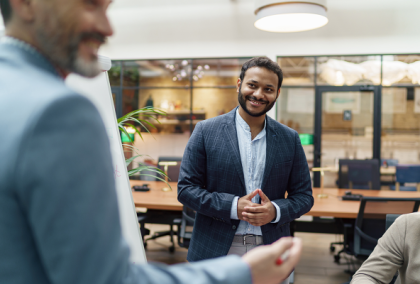 Smiling man in suit speaking to colleagues around a conference table in modern office.