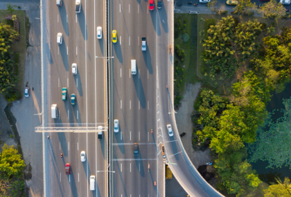 Aerial photograph of a multi-lane highway interchange with cars and green roadside vegetation.