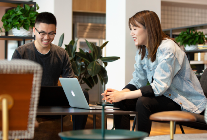 Two people seated at a café table, one with a laptop and coffee, the other holding a tablet