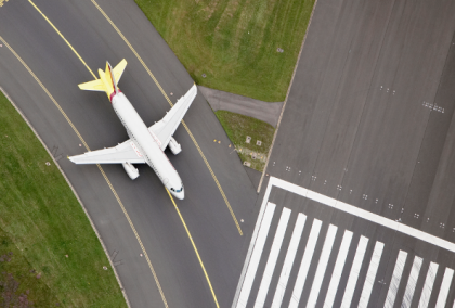 Aerial photo of white passenger jet with yellow tail taxiing alongside runway