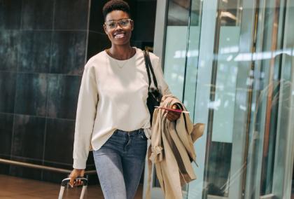 Woman in white blouse and jeans holding trench coat and purse in glass-walled corridor