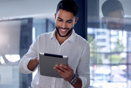 Young bearded man in gray shirt smiling while using tablet in modern office