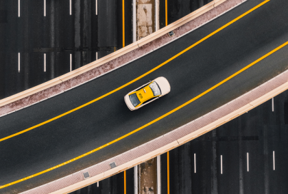 Aerial view of curved highway overpass with a yellow taxi in center lane