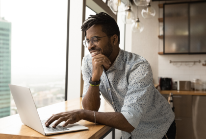 Bearded man in glasses leaning on hand while using laptop at cafe window