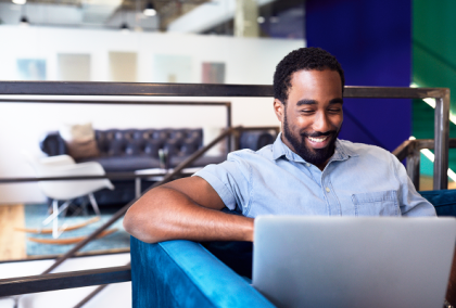 Smiling bearded man working on a laptop in a modern office lounge.