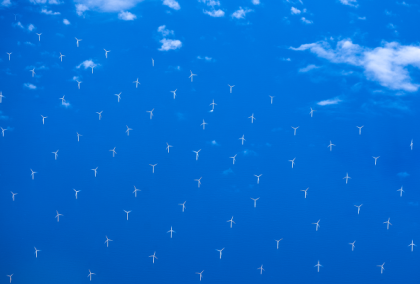 Aerial view of offshore wind turbines on bright blue sea under scattered clouds