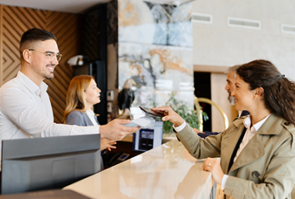 A woman business traveller at a hotel front desk discussing ancillary charges with the desk clerk