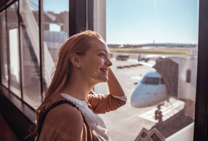 Young woman in airport terminal looking out at waiting airplane on the runway