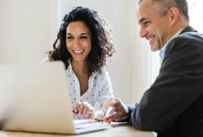 Businesswoman and man smiling while working on a laptop in a bright office.