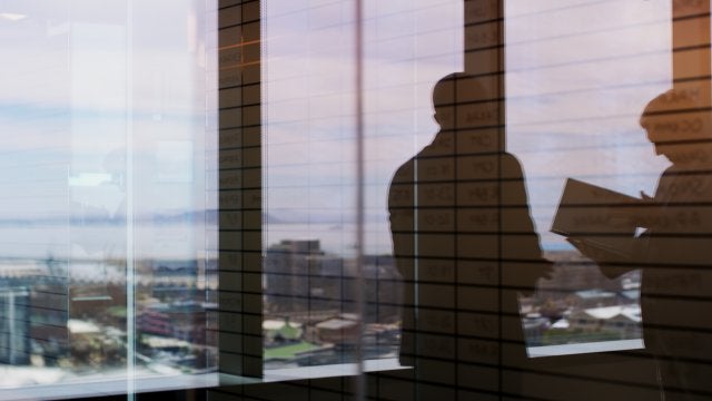 Ejecutiva observando la ciudad desde un edificio corporativo mientras analiza decisiones estratégicas para el negocio.
