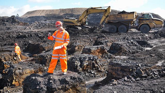 Miner standing in quarry with machinery behind