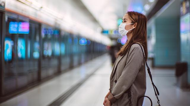 Woman at train station wearing mask.