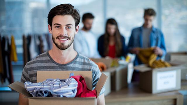 Male with donations box of clothes looking at camera with other volunteers in background
