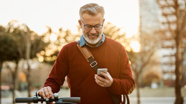 Man looking at phone on sidewalk with bicycle.