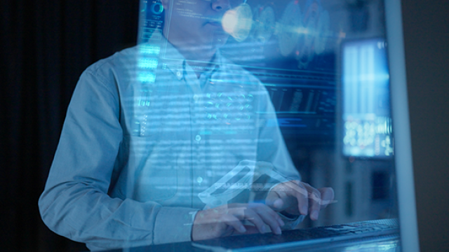 A person typing on a laptop, surrounded by digital data on a screen.