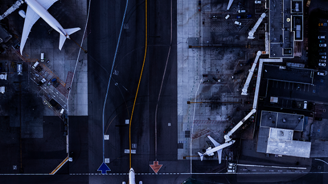 Aerial view of airport tarmac with airplanes at gates beside terminal.