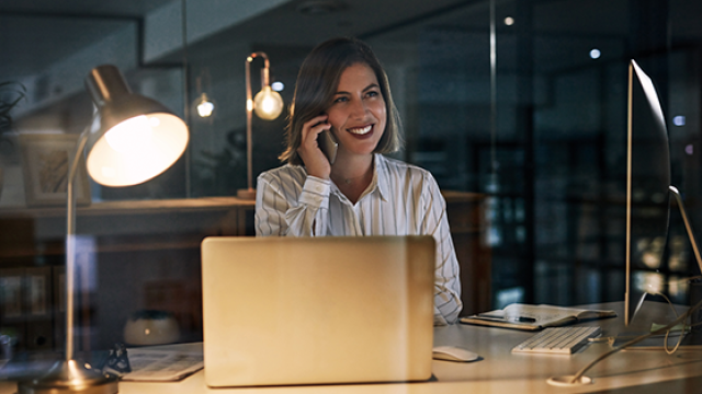Businesswoman talking on phone while seated at desk with open laptop in office.