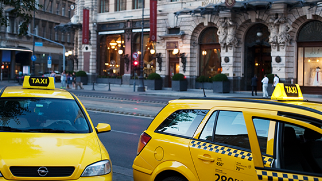 Two yellow taxis parked on a city street in front of a historic building.