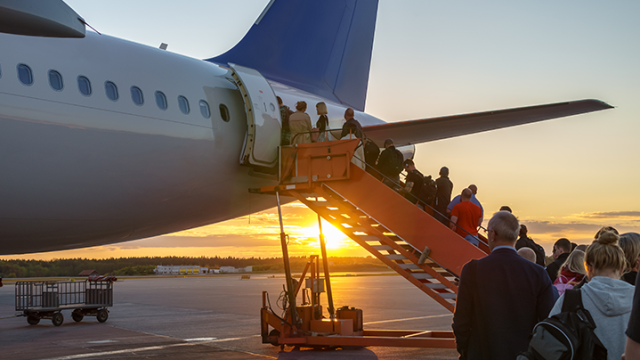 Passengers ascending plane stairs at sunset on an airport tarmac