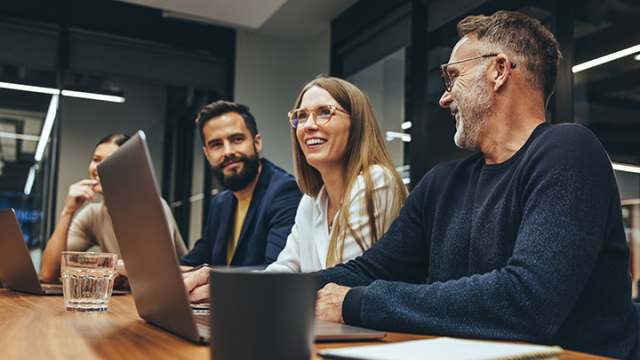 Group of people at a board meeting, around a laptop