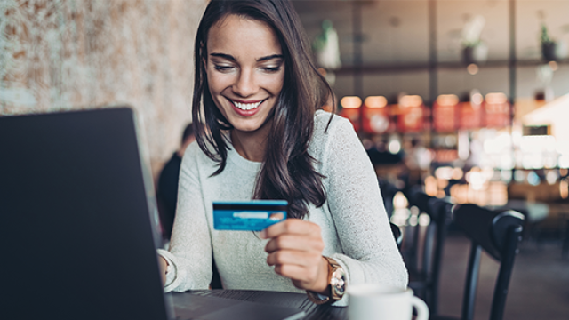 Woman looking at credit card while booking travel online.