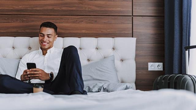 Man sitting on hotel bed on phone smiling