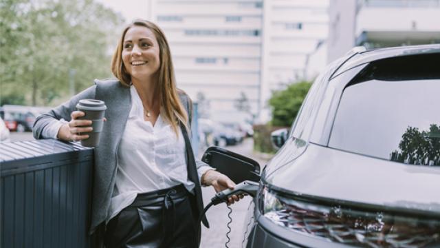 Women holding a cup of coffee filling up her car with petrol 