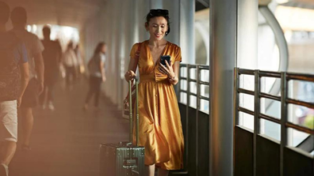 Smiling traveller walking through an airport with luggage whilst looking at phone