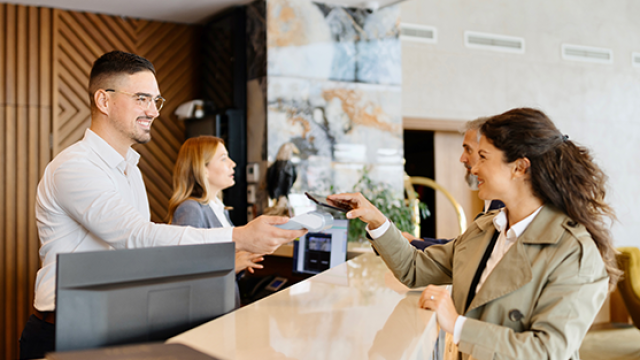 A woman business traveller at a hotel front desk discussing ancillary charges with the desk clerk