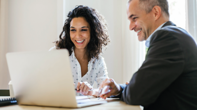 Businesswoman and man smiling while working on a laptop in a bright office.