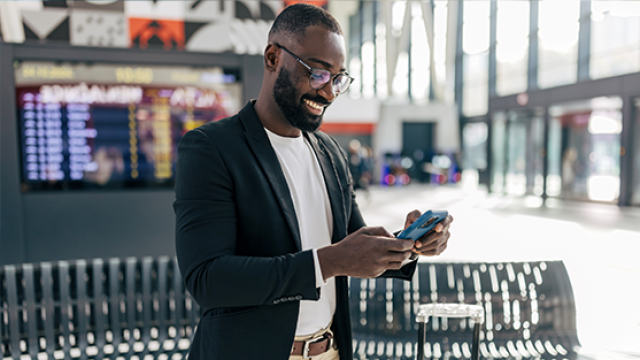 Smiling man in blazer checking his phone and boarding pass in an airport terminal