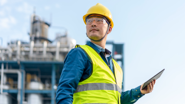 Engineer in yellow hard hat and reflective vest holding tablet at industrial plant