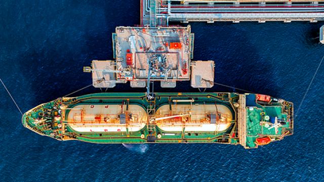 Aerial view of tanker with two cylindrical tanks docked at industrial pier over blue water