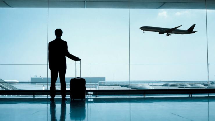 Man at airport with suitcase looking out at landing plane