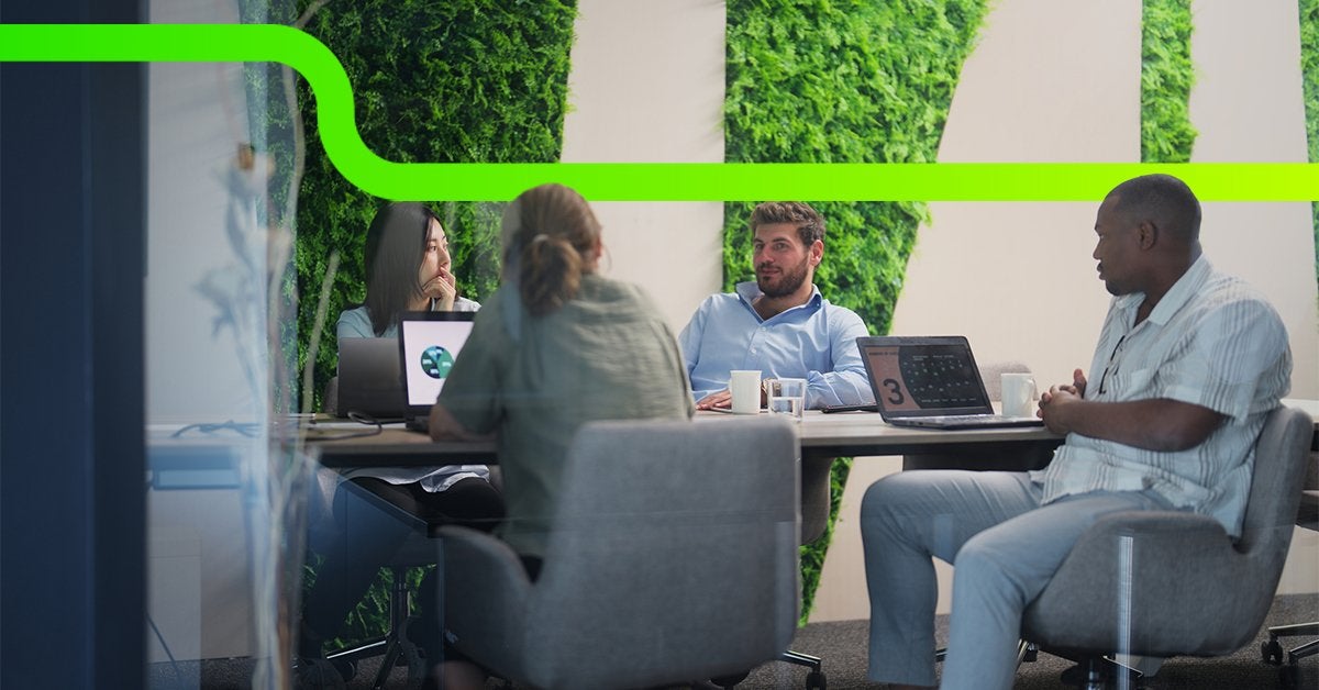 Equipo corporativo en reunión estratégica frente a un muro verde vegetal, conversando sobre sostenibilidad y decisiones empresariales.