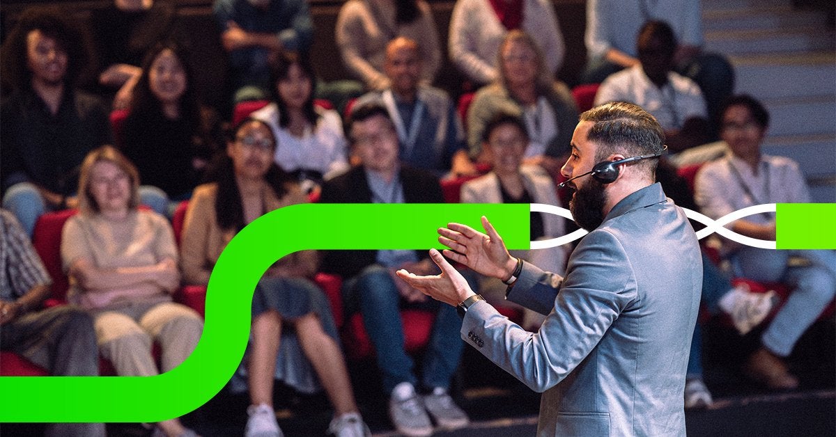 Speaker presentando frente a una audiencia en un evento corporativo, con asistentes atentos en un auditorio durante una experiencia en vivo.