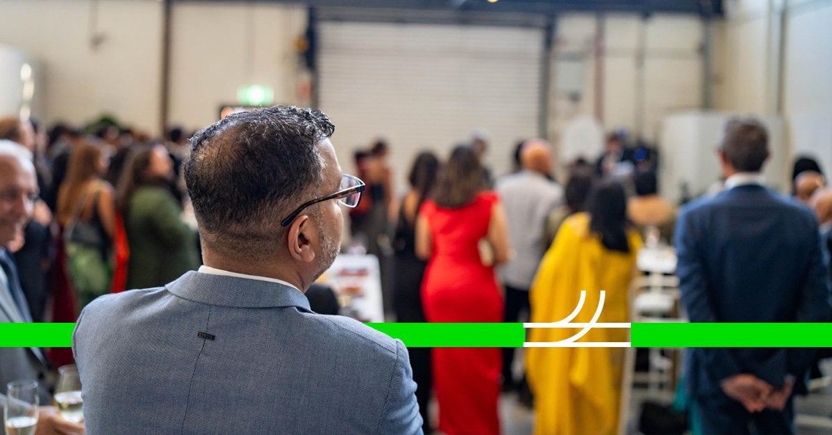 Ejecutivo observando un evento corporativo desde la audiencia en un entorno profesional y elegante.