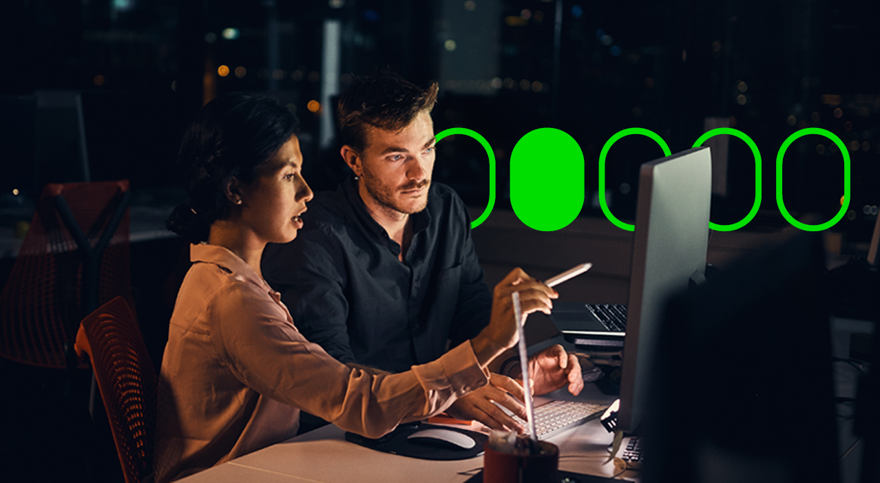 A man with a beard, and a lady in a brown shirt, looking at a mac screen, talking