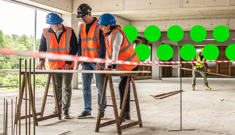 3 people standing on construction site looking at plans in highvis
