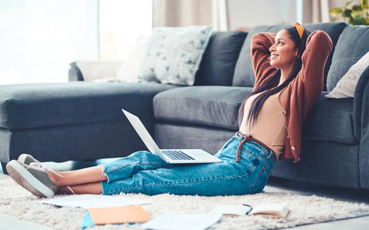 Relaxed women sitting on the floor with a laptop on her lap smiling into the distance