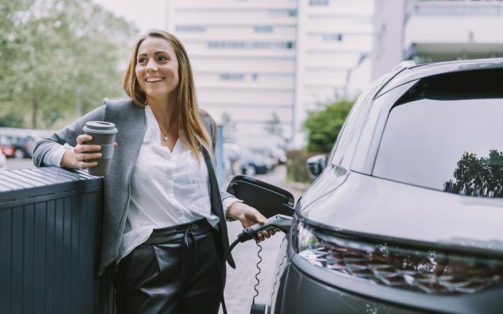 Smiling women holding a cup of coffee filling up her car with petrol