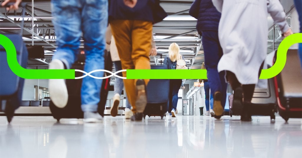 Viajeros corporativos caminando por un aeropuerto internacional con equipaje de mano durante un viaje de negocios.