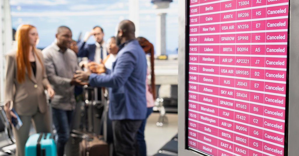 Pantalla de aeropuerto con múltiples vuelos cancelados mientras viajeros corporativos buscan alternativas para continuar sus itinerarios.