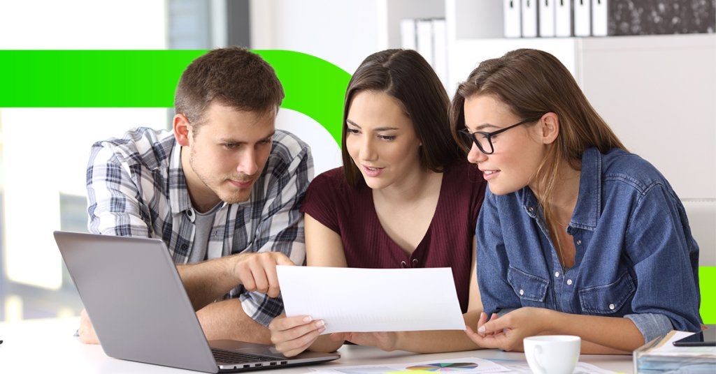 Tres colaboradores analizando documentos y datos en una laptop, simbolizando la búsqueda estructurada de sedes y la toma de decisiones corporativas.